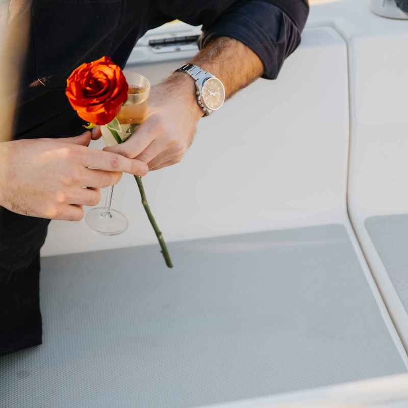 Person holding a red rose and a glass of champagne on a boat.
