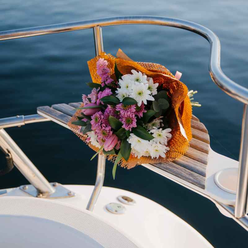 Bouquet of flowers on the edge of a boat with a calm water backdrop.