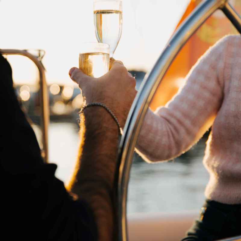 Two people toasting with champagne glasses on a boat during sunset.
