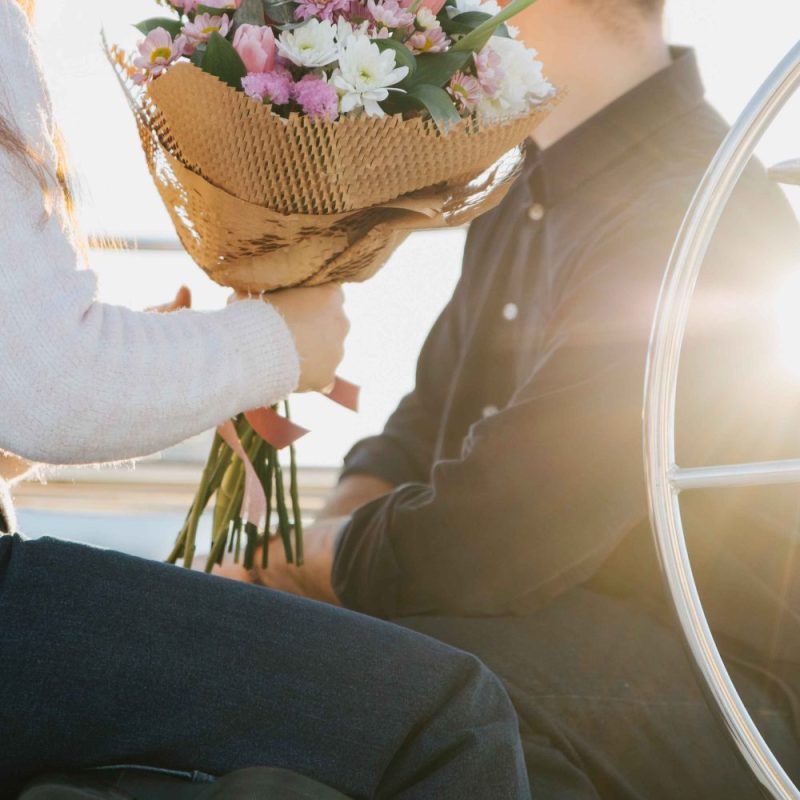 Person holding a bouquet of flowers on a sunny day with another person sitting nearby.