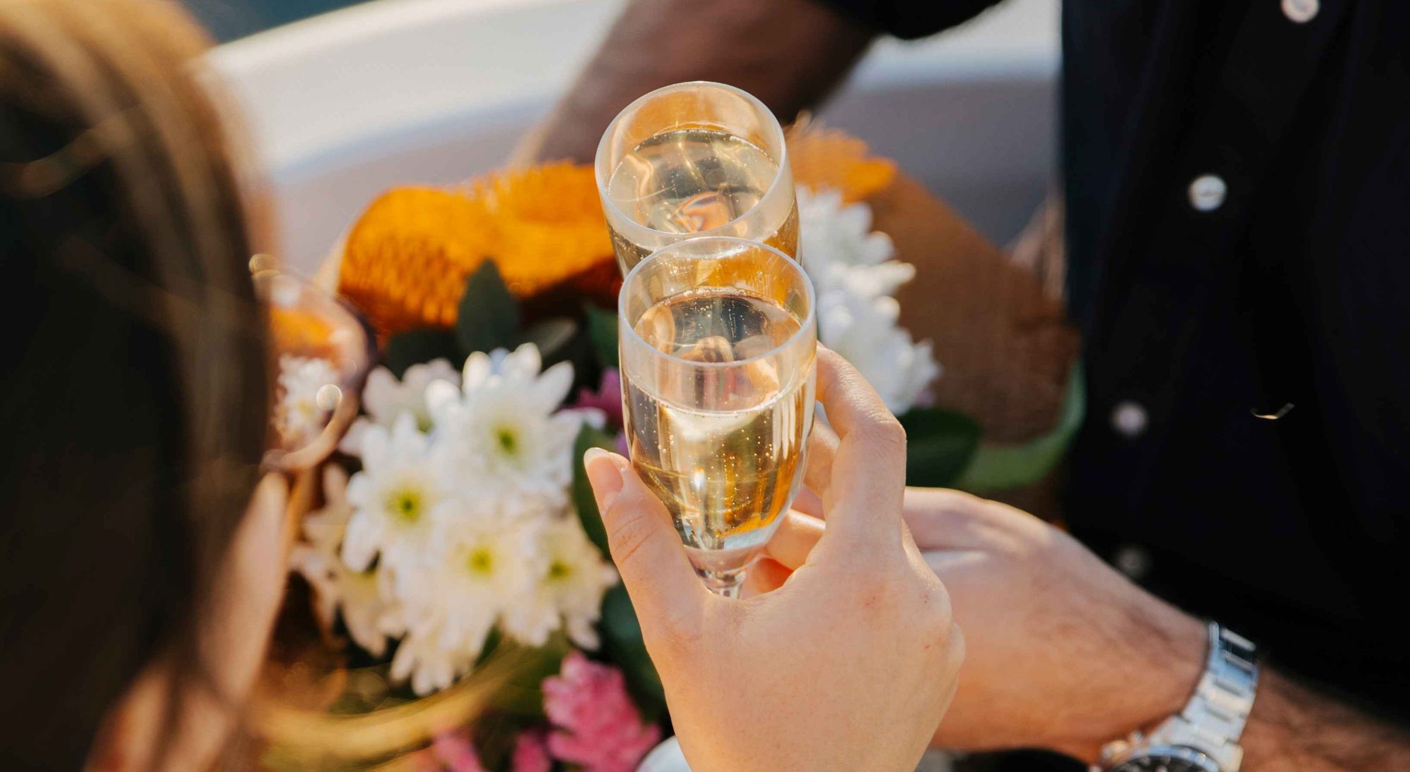 Two people clinking champagne glasses near a bouquet of flowers.