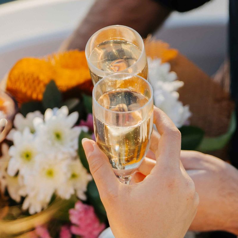 Two people clinking champagne glasses near a bouquet of flowers.