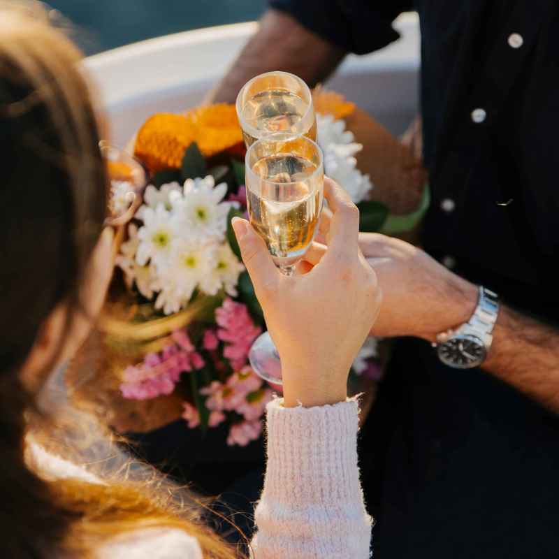 Two people clinking champagne glasses near a bouquet of flowers.