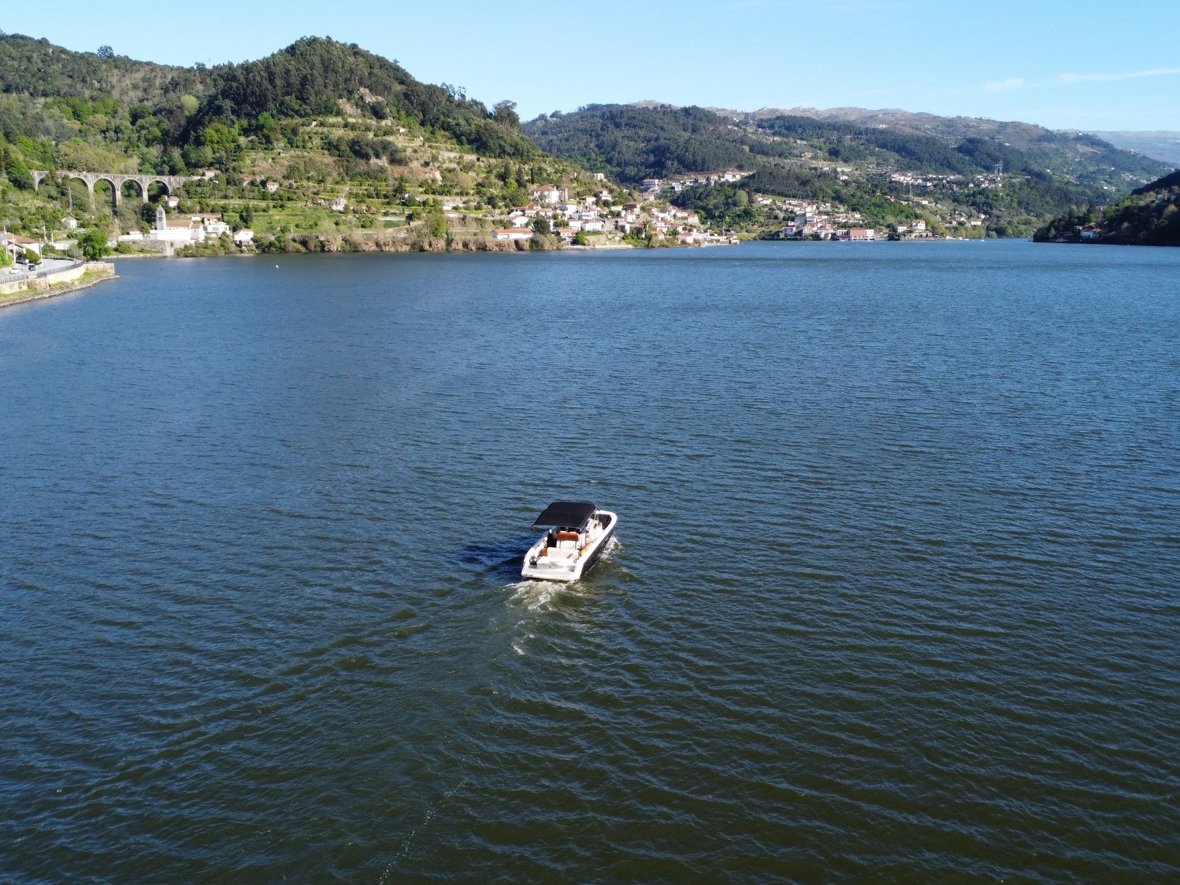 A boat on a wide river surrounded by green hills and distant buildings.