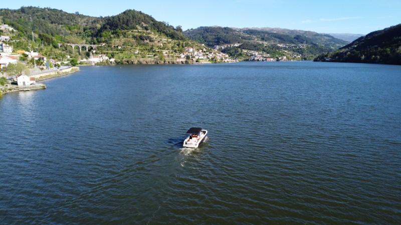 A boat on a wide river surrounded by green hills and distant buildings.