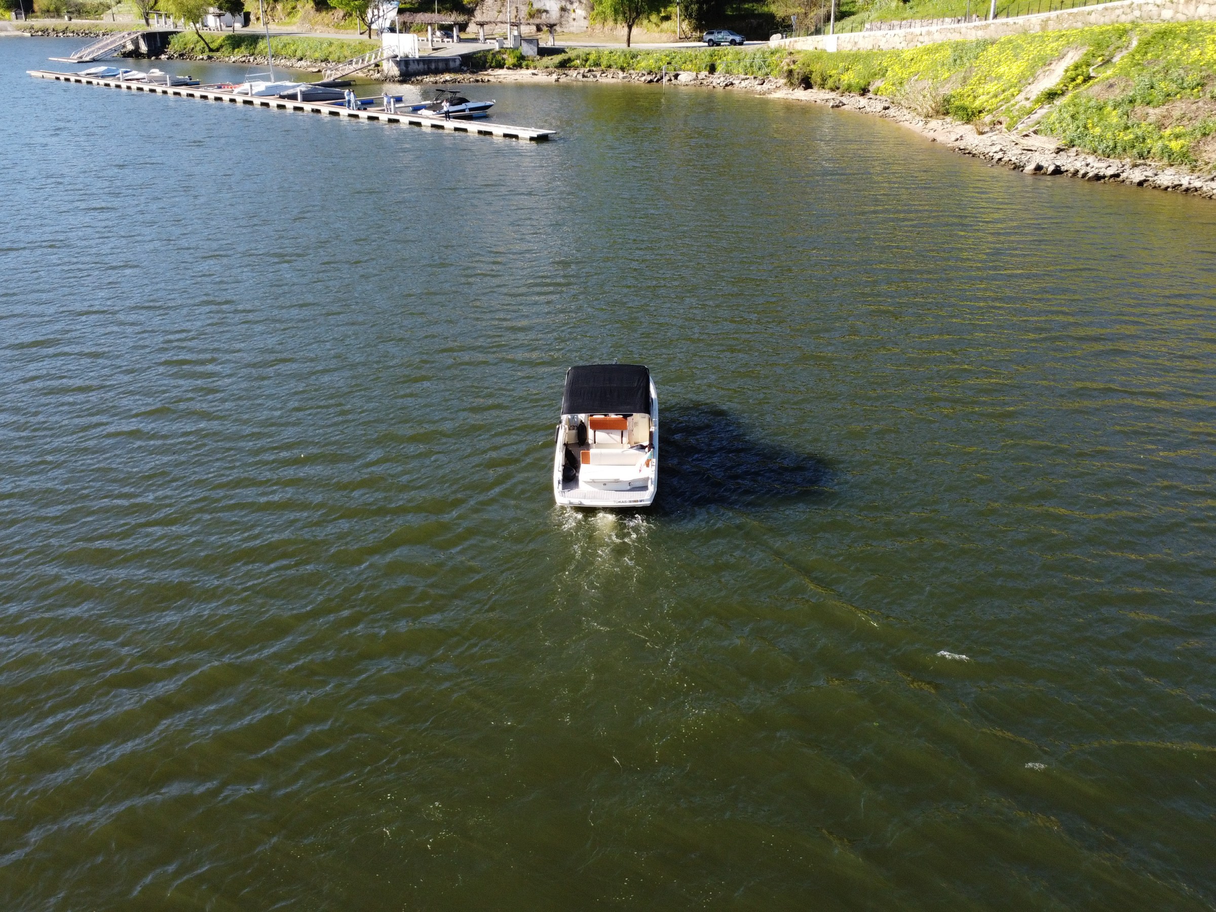 Small boat with canopy on calm water near shoreline and docks.