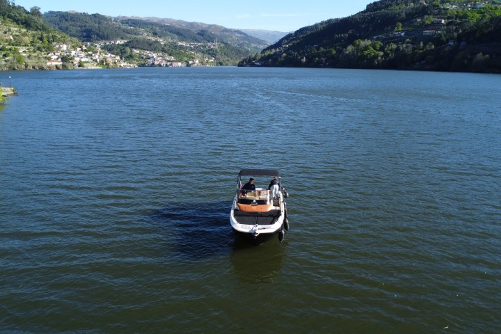 Small boat with people in the middle of a wide river, surrounded by hills and distant town.