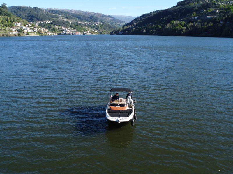 Small boat with people in the middle of a wide river, surrounded by hills and distant town.