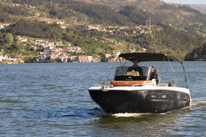Small motorboat on river with person, hills and houses in background.