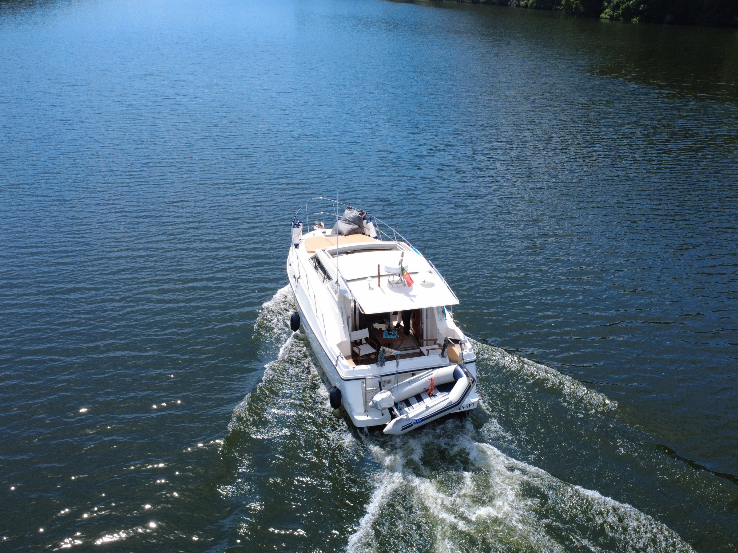 Aerial view of a white boat cruising on a calm lake with trees in the background.