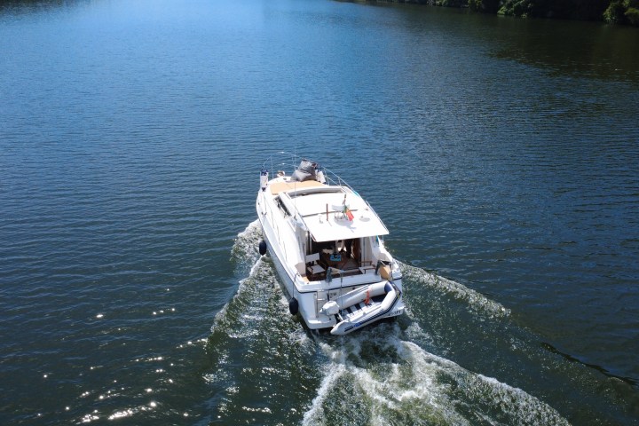Aerial view of a white boat cruising on a calm lake with trees in the background.