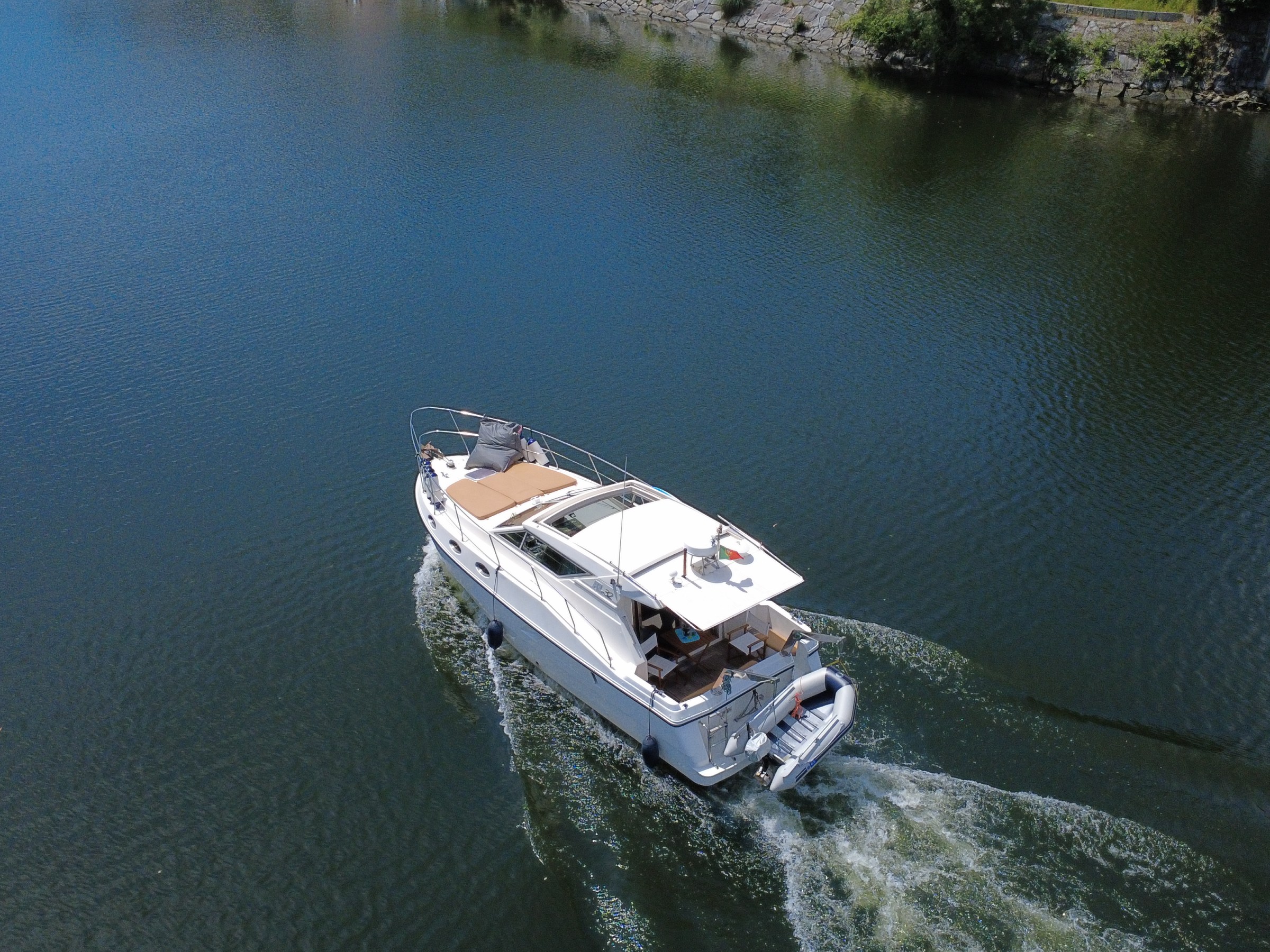 Small white motorboat cruising on calm water near a rocky shoreline.