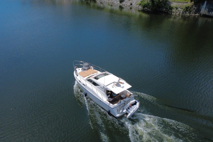 Small white motorboat cruising on calm water near a rocky shoreline.