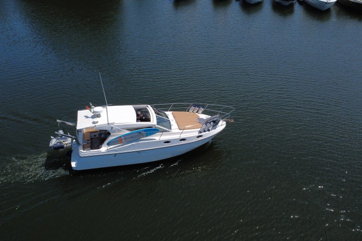 White motorboat cruising on calm water near a row of docked boats.