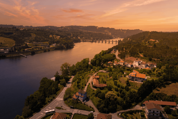 Aerial view of a river with a bridge and houses at sunset.