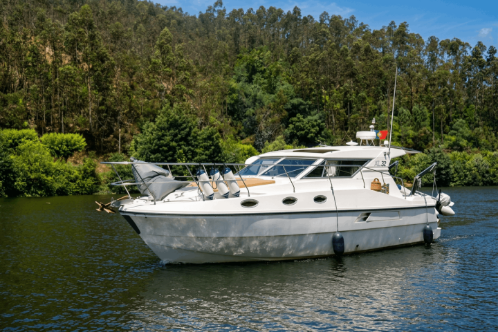 White yacht on a calm river with a forested hillside in the background.
