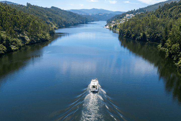Boat on a wide river flanked by green forests and hills under a blue sky.