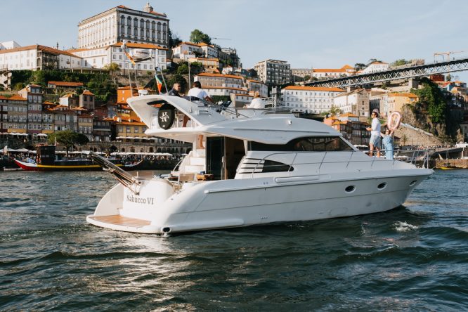 White yacht on river with historic city buildings and bridge in background.