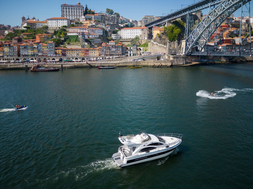 White boat cruising under the great arch of the Luís I Bridge on the Douro River on a sunny day