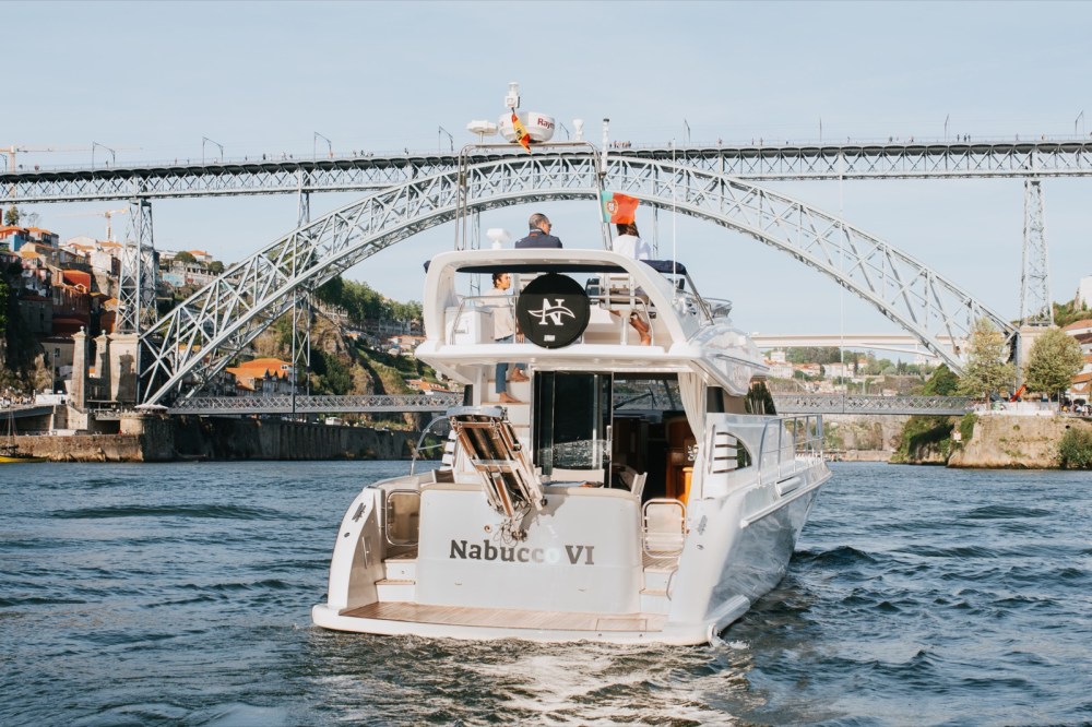 Motorboat named Nabucco VI on a river with a metal bridge in the background.