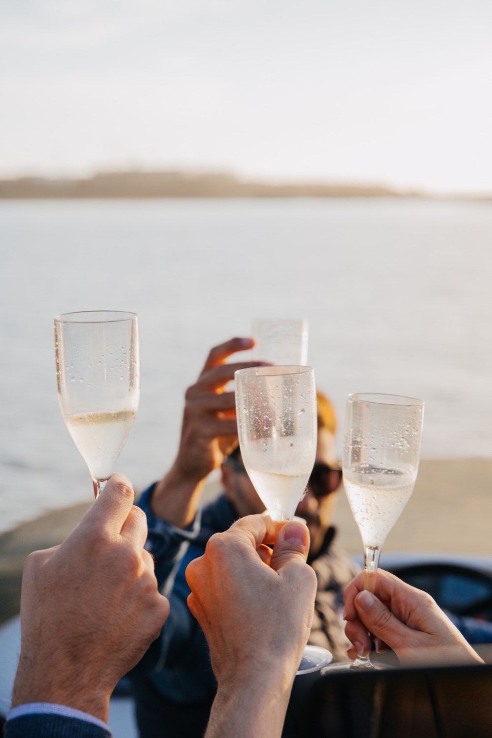 Mãos a erguer copos de vinho num brinde a bordo, com o Rio Douro em segundo plano ao fim da tarde