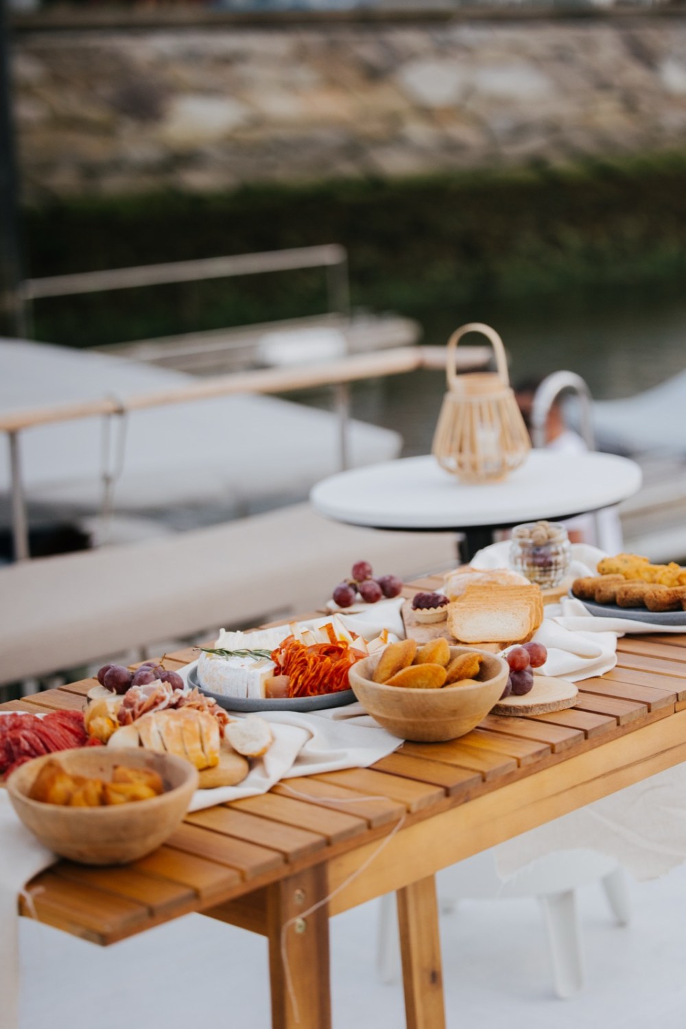 Outdoor table with assorted snacks and fruits near waterfront.