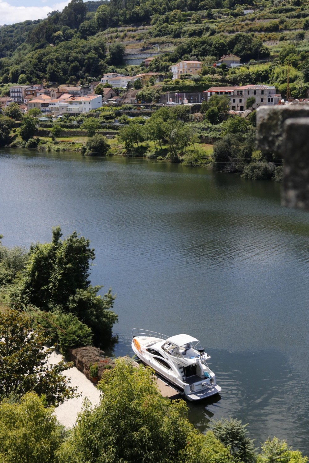 White boat cruising around a bend of the Douro River, with green hillsides and a small village on the bank
