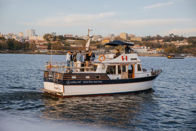 Small tour boat with people on a river, cityscape in background.