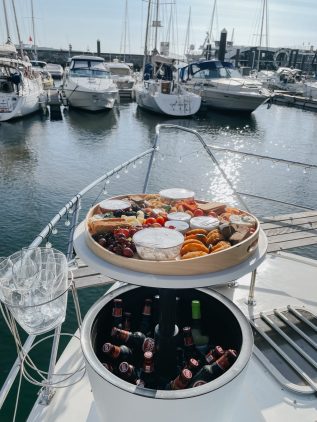Tábua de queijos, enchidos, pão e frutos secos disposta no convés de madeira de um barco no Douro