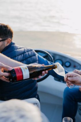Crew member pouring wine into a glass aboard a boat on the Douro River, with the river behind