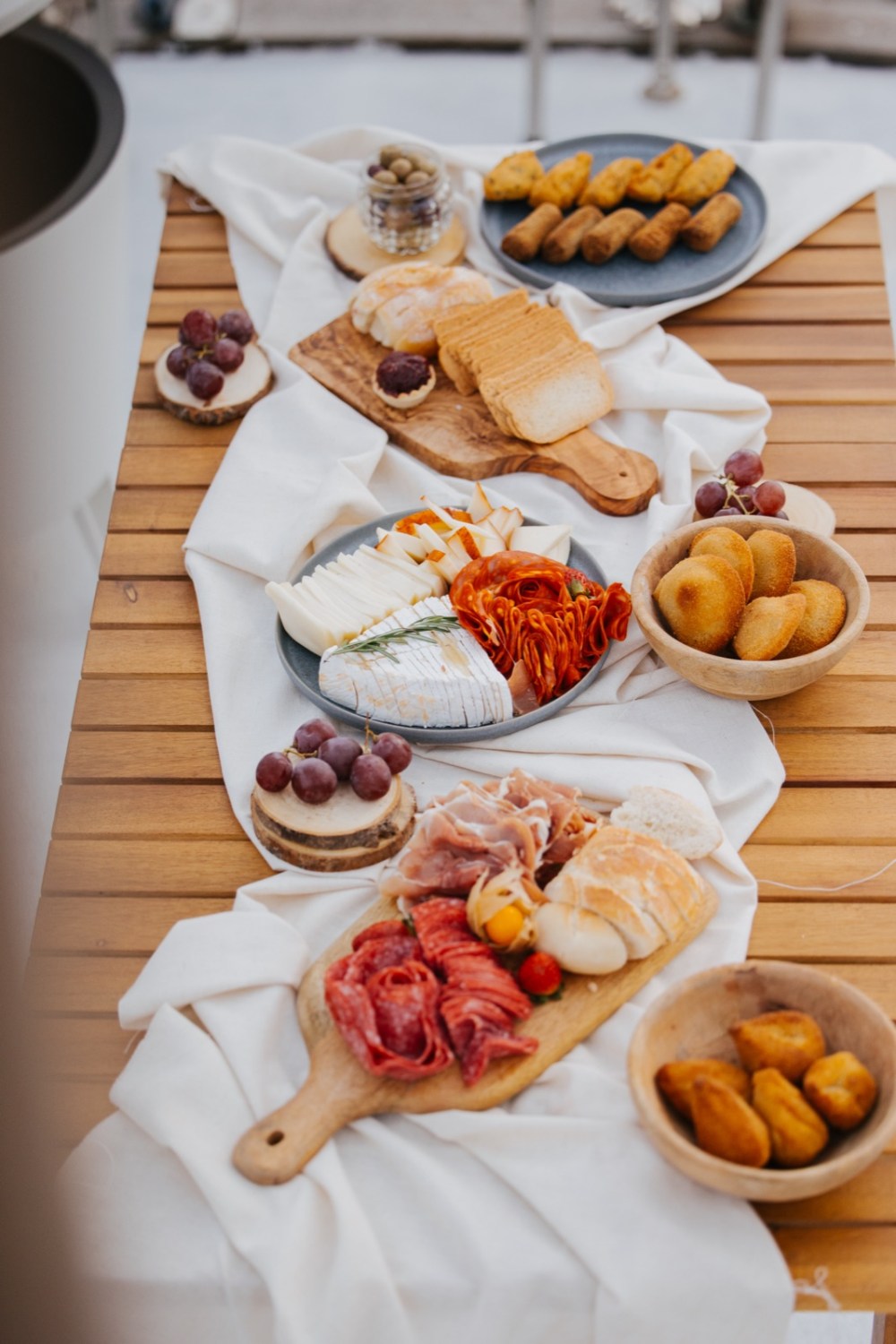 Board of cheeses, cured meats, bread and nuts laid out on the wooden deck of a boat on the Douro