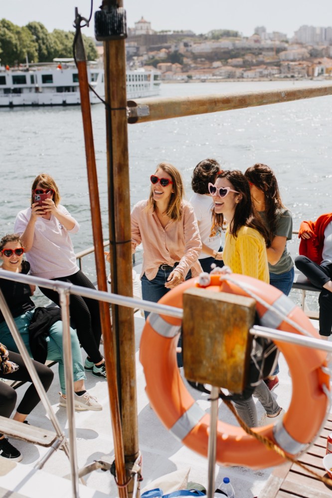Group of people on a boat, some taking photos and wearing sunglasses, with a lifebuoy in foreground.