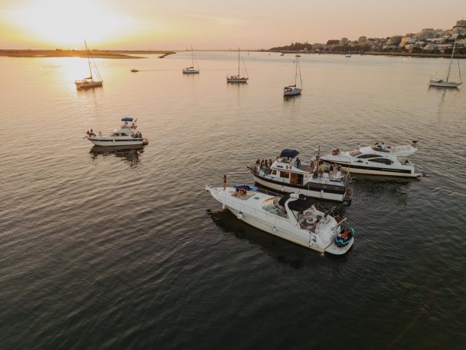 Boats floating on a calm river at sunset, with houses in the background.