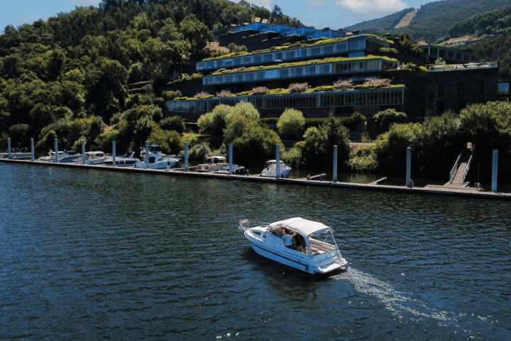 A boat on a river with hillside buildings and greenery in the background.