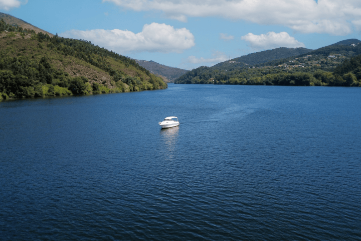 A small boat on a wide lake surrounded by hills under a cloudy sky.