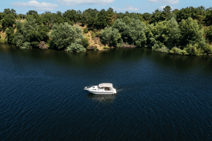 A small white boat on a serene lake surrounded by lush green trees.